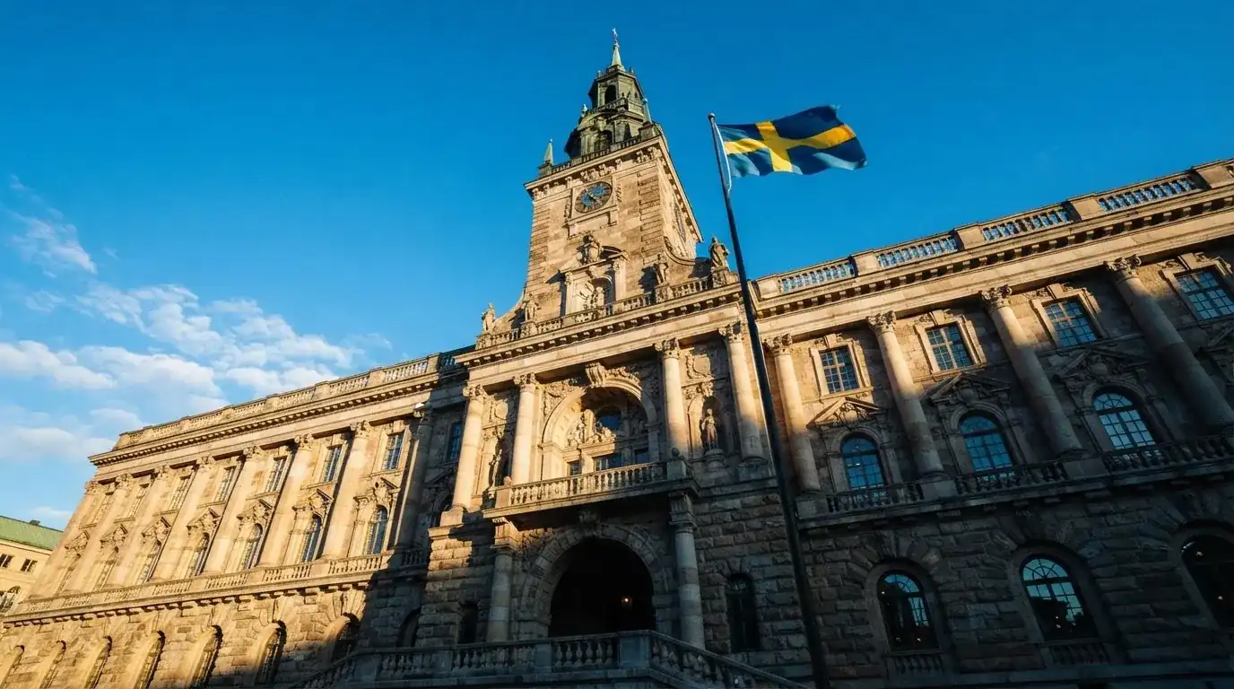 Ett gammalt stadshus i sten fotograferat underifrån mot en klarblå himmel, med den svenska flaggan som fladdrar ovanför entrén.